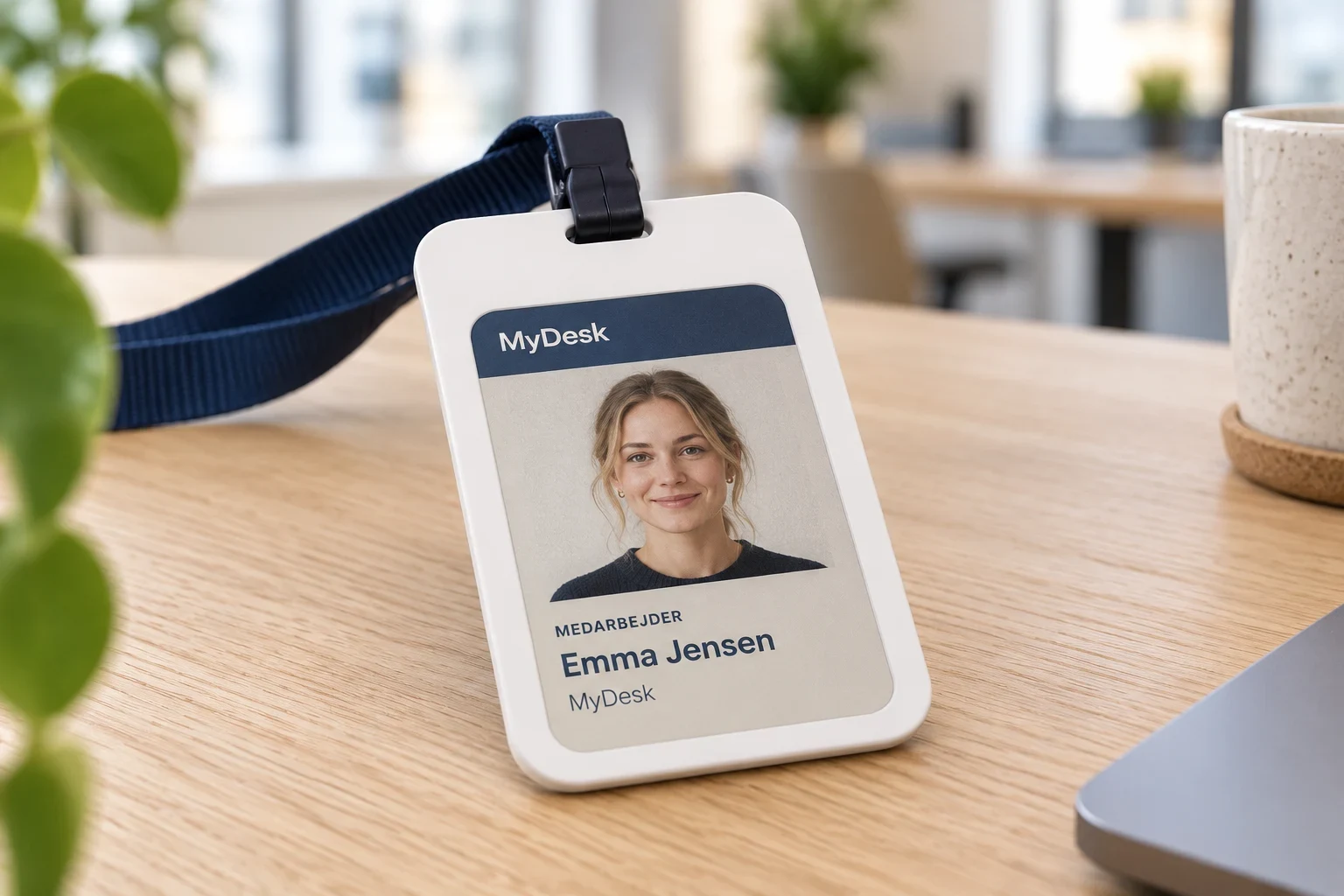 Illustratie van de witte E-Ink-medewerkerskaart van MyDesk met foto, naam en logo op een bureau