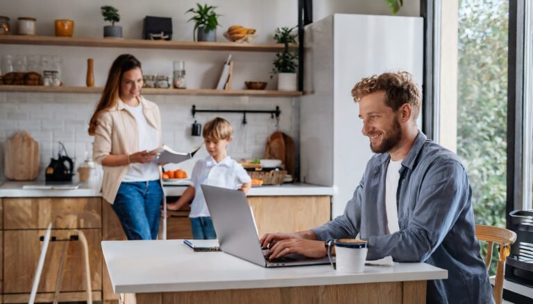 Hybrid workplace, man working on laptop in kitchen with his wife and son.